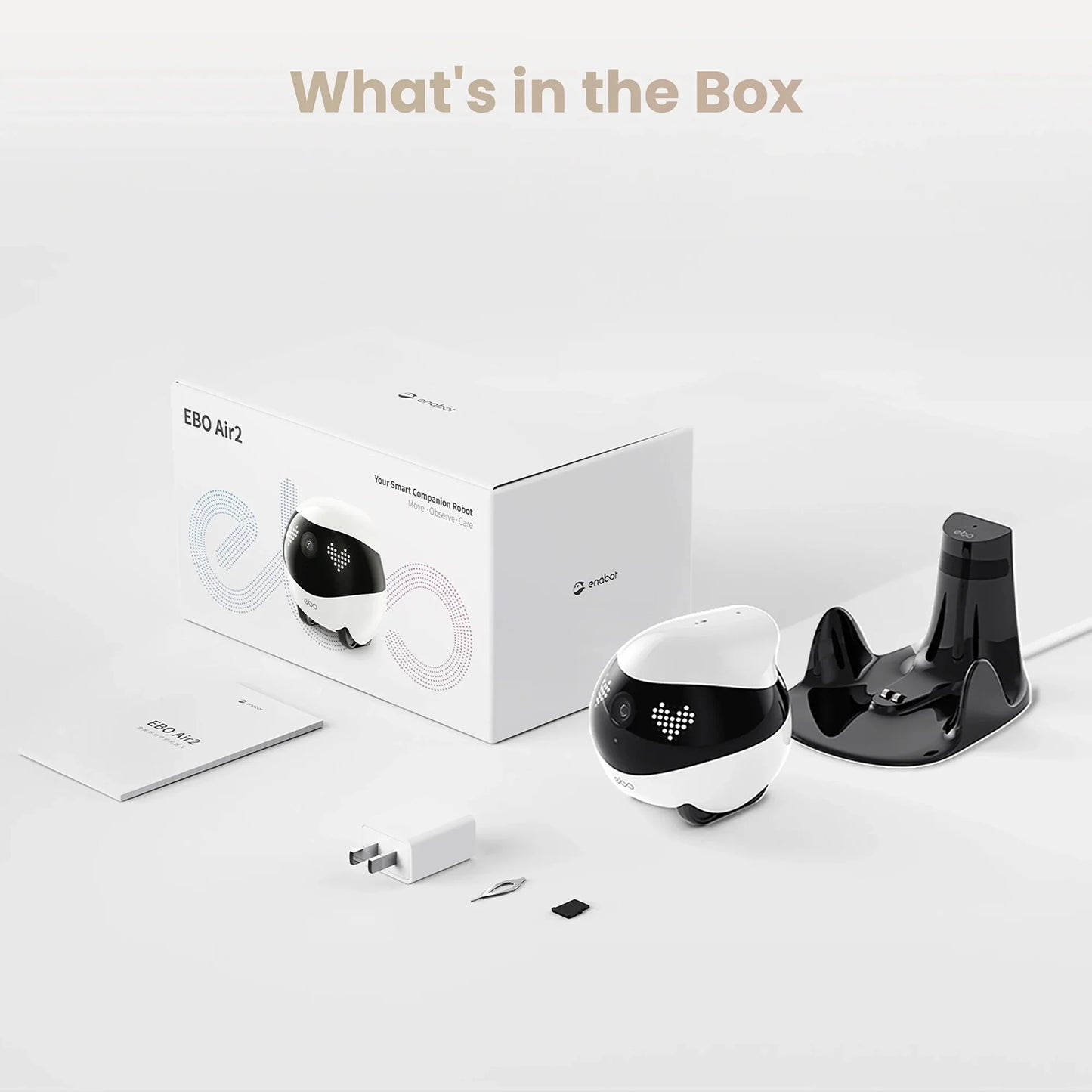 smart tech store Canada. premium tech accessories Canada. Enabot Ebo Air 2 Companion Robot. Gallery image 4. A compact, round robot, primarily white with a black top, is positioned to the left of a white box labeled "EBO Air2" in colorful text. The robot features a small camera and LED lights on its front. To the right, a glossy black charging dock is visible, along with a white power adapter, a small tool, and a memory card.