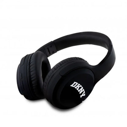 future tech gadgets Canada. premium tech accessories Canada. DKNY Headphones Bluetooth. Gallery image 2. The black over-ear headphones are angled slightly to the right, showcasing their plush ear cushions and adjustable headband. The left ear cup features a prominent white "DKNY" logo, while the right side has visible buttons for controls. The background is a seamless white, enhancing the sleek design of the headphones.