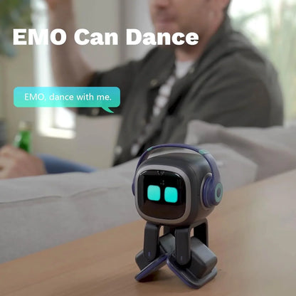 smart tech store Canada. premium tech accessories Canada. Living AI EMO AI Desktop Pet Companion Robot. Gallery image 5. A small, cartoonish robot named EMO is positioned on a wooden table, facing slightly to the right. It has a glossy black body with bright blue eyes and purple accents on its headphones. The background features a blurred figure of a person sitting on a couch, raising their hand, suggesting interaction. Soft, natural light illuminates the scene, creating a warm atmosphere.