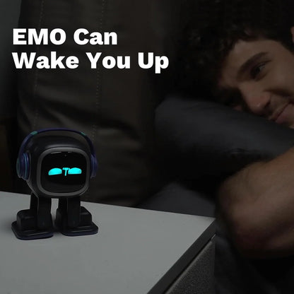 smart tech store Canada. premium tech accessories Canada. Living AI EMO AI Desktop Pet Companion Robot. Gallery image 4. A small, cartoonish robot with a round face and blue headphones sits on a light-colored bedside table. Its face features glowing blue eyes and a simple mouth, suggesting a friendly demeanor. In the background, a young man rests on a dark pillow, smiling as he looks at the robot.
