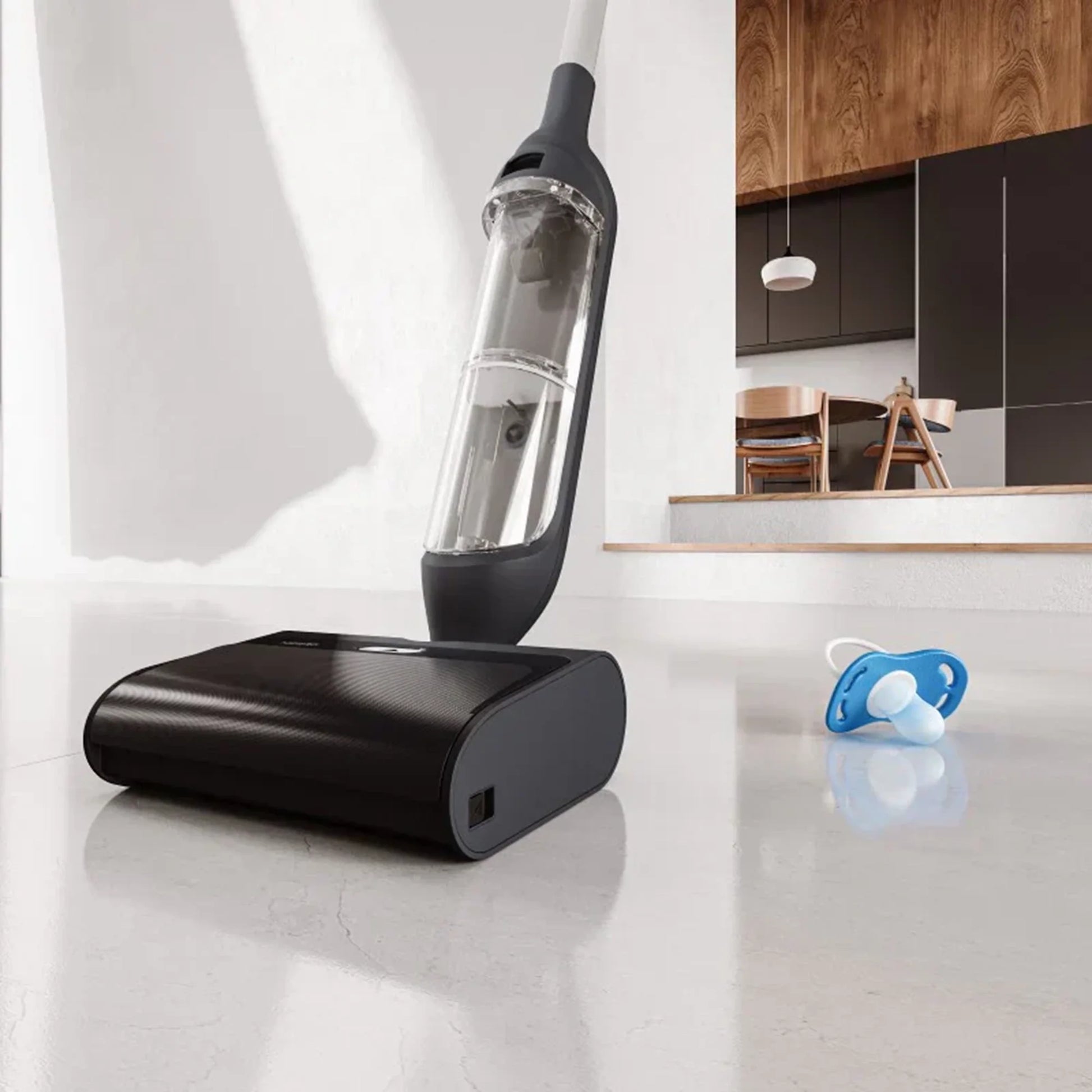 future tech gadgets Canada. smart tech store Canada. HiZero F300 All-in-One Bionic Floor Cleaner. Gallery image 2. A sleek, black vacuum cleaner is positioned at an angle in the foreground, with its transparent dust container prominently displayed. The vacuum rests on a smooth, light-colored floor, reflecting soft light that highlights its glossy finish. In the background, a modern kitchen is visible, featuring wooden cabinetry and a dining area with chairs.