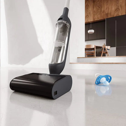 future tech gadgets Canada. smart tech store Canada. HiZero F300 All-in-One Bionic Floor Cleaner. Gallery image 2. A sleek, black vacuum cleaner is positioned at an angle in the foreground, with its transparent dust container prominently displayed. The vacuum rests on a smooth, light-colored floor, reflecting soft light that highlights its glossy finish. In the background, a modern kitchen is visible, featuring wooden cabinetry and a dining area with chairs.
