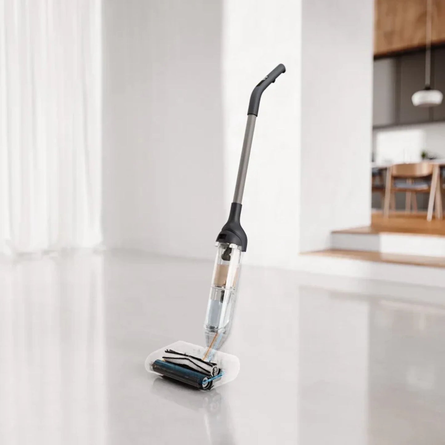 future tech gadgets Canada. smart tech store Canada. HiZero F300 All-in-One Bionic Floor Cleaner. Gallery image 3. A sleek, upright floor cleaner is positioned at an angle in the foreground, with its transparent water tank prominently visible. The cleaner features a black handle and a silver pole, resting on a white cleaning pad that has a dark roller brush. The background shows a softly lit, modern kitchen with wooden accents and a dining area, enhancing the product's contemporary feel.