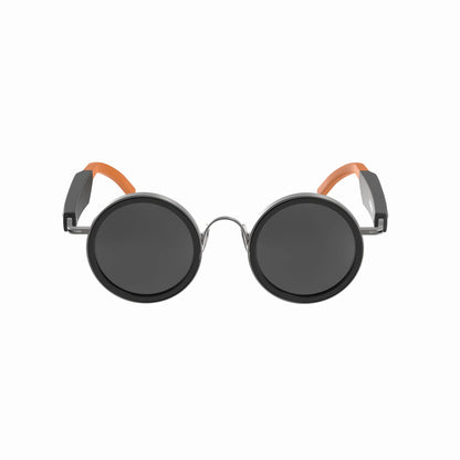 future tech gadgets Canada. smart tech store Canada. Techtron Oracle Smart Sunglasses. Gallery image 1. The sunglasses are centered in the frame, facing directly forward. They feature large, round black lenses with a glossy finish. The frame is primarily black with a shiny metallic bridge connecting the lenses. The arms of the sunglasses have a sleek design, with the left arm in matte black and the right arm accented by a bright orange rubber tip.