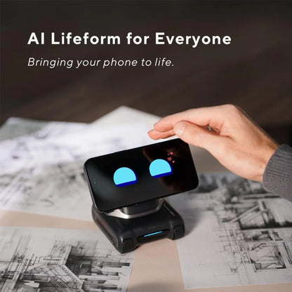 future tech gadgets Canada. smart tech store Canada. LOOI L01 AI Desk Companion Robot. Gallery image 3. A smartphone with a cartoonish face displaying blue eyes is positioned on a small, black device that resembles a stand. A hand reaches toward the phone, suggesting interaction. The background features sketches and blueprints scattered on a light-colored surface, creating a creative workspace atmosphere. Soft, natural lighting highlights the device and phone, casting gentle shadows.