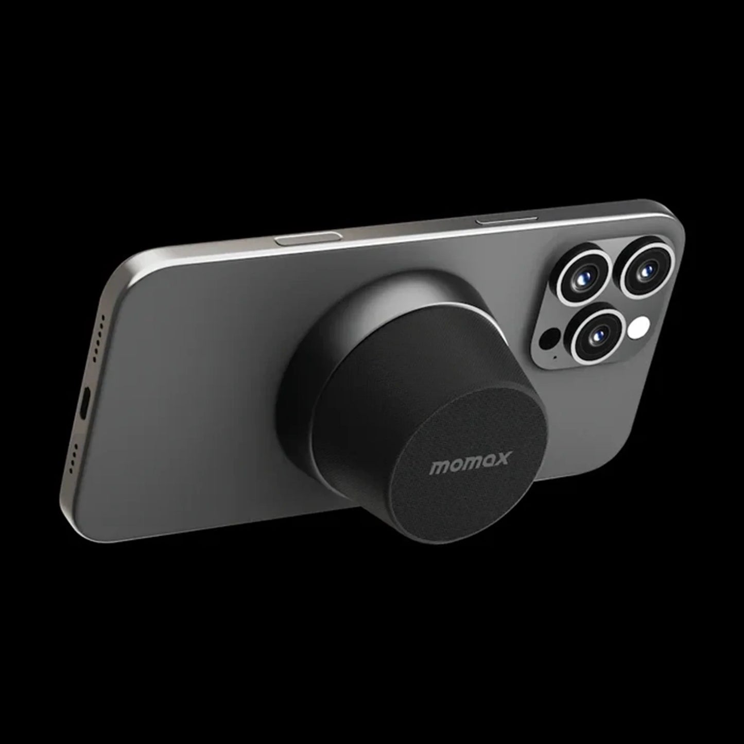 future tech gadgets Canada. premium tech accessories Canada. Momax 1-Vibe Go Magnetic Wireless Speaker. Gallery image 9. The image features a sleek, dark gray smartphone positioned at an angle against a black background. A circular, black accessory with a textured surface is attached to the back of the phone, prominently displaying the "momax" logo. The phone's camera module, which includes three lenses, is visible on the right side.