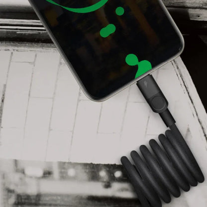 future tech gadgets Canada. premium tech accessories Canada. Momax Mag.Link 66W Usb-A To Usb-C Magnetic Cable 1M. Gallery image 2. A smartphone is positioned at the top of the frame, displaying a vibrant green graphic on its screen. The device is plugged into a coiled black charging cable, which lies on a textured surface that appears to be a light-colored wooden table. The cable's connector is visible, featuring a small button and a lightning bolt symbol.