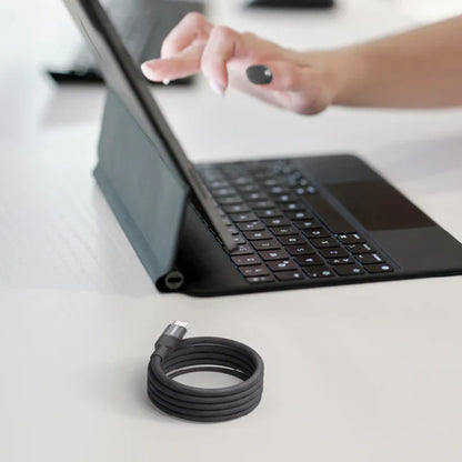 future tech gadgets Canada. premium tech accessories Canada. Momax Mag.Link 66W Usb-A To Usb-C Magnetic Cable 1M. Gallery image 5. A sleek black tablet is propped up at an angle on a light-colored desk, showcasing a detachable keyboard with backlit keys. A hand with a dark nail polish is reaching towards the tablet's screen. In the foreground, a coiled black USB-C charging cable rests neatly on the desk.