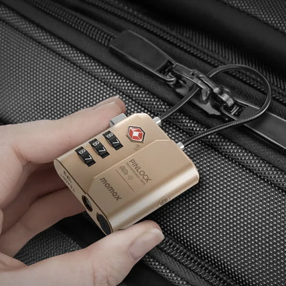 future tech gadgets Canada. smart tech store Canada. Momax Pinlock TSA Padlock Find My Location. Gallery image 1. A gold combination lock is held in a hand, with its cable looped through a zipper pull on a textured black suitcase. The lock features three rotating dials displaying the numbers 8, 7, and 7, along with a red logo on the front. The background is a close-up of the suitcase's fabric, emphasizing its durable material.