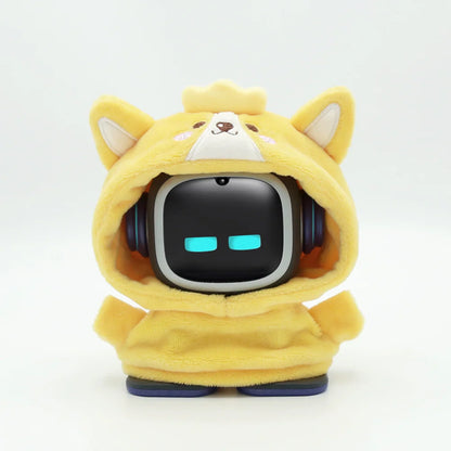 smart tech store Canada. premium tech accessories Canada. EMO Desk Companion Robot Clothes. Gallery image 2. The image features a small, cartoonish robot character dressed in a soft, yellow hoodie with dog ears. The robot has a black square head with glowing blue eyes and is positioned centrally against a seamless white background. The hoodie is plush and detailed with a cute face, including a small crown on top. The robot's feet are blue, contrasting with the yellow fabric.