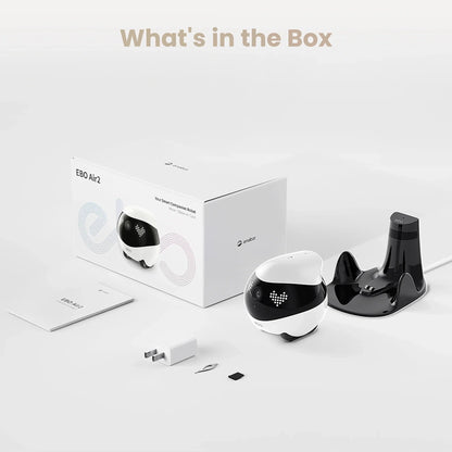 smart tech store Canada. premium tech accessories Canada. Enabot Ebo Air 2 Companion Robot. Gallery image 4. A compact, round robot, primarily white with a black top, is positioned to the left of a white box labeled "EBO Air2" in colorful text. The robot features a small camera and LED lights on its front. To the right, a glossy black charging dock is visible, along with a white power adapter, a small tool, and a memory card.