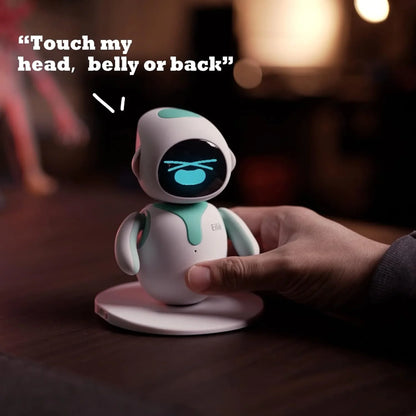 smart tech store Canada. premium tech accessories Canada. Eilik Desktop Companion AI Robot. Gallery image 3. A small, friendly robot figure stands on a circular white base, centered in the frame. The robot has a glossy black face with blue digital eyes and a white body accented with teal highlights on its head and chest. A hand gently touches the robot's side, indicating interaction. The background is softly blurred with warm lighting, creating a cozy atmosphere.
