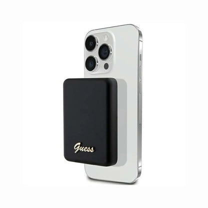 cutting edge electronics online Canada. premium tech accessories Canada. Guess Powerbank Magsafe Metal Script Logo 5000mAh 15W Black. Gallery image 3. A sleek black portable charger is magnetically attached to the back of a white smartphone, showcasing a modern design. The charger features a gold "Guess" logo on the front, adding a touch of elegance. The smartphone's camera lenses and buttons are visible on the side, while the background is a seamless white, emphasizing the products.