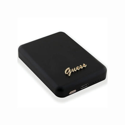 cutting edge electronics online Canada. premium tech accessories Canada. Guess Powerbank Magsafe Metal Script Logo 5000mAh 15W Black. Gallery image 2. The image features a sleek, rectangular black power bank positioned at a slight angle, showcasing its smooth matte finish. A gold "Guess" logo is prominently displayed on the front, adding a touch of elegance. On the side, a small button and a USB-C port are visible, along with a row of indicator lights.