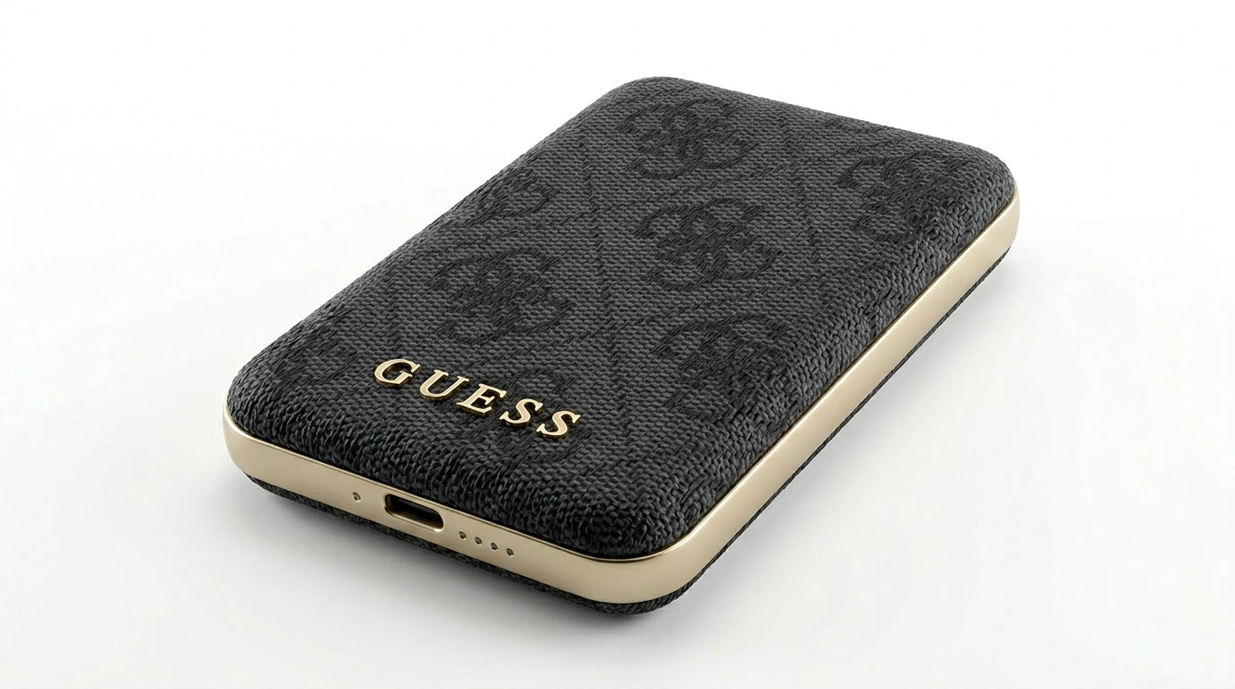 future tech gadgets Canada. premium tech accessories Canada. Guess BP MagSafe Case + PWB 5000mAh 4G. Gallery image 8. The image features a black phone case with a textured fabric surface, angled slightly to showcase its design. The case is adorned with a subtle pattern and the word "GUESS" prominently displayed in gold lettering along the bottom edge. The sides of the case are finished in a glossy gold trim, contrasting with the matte black texture.