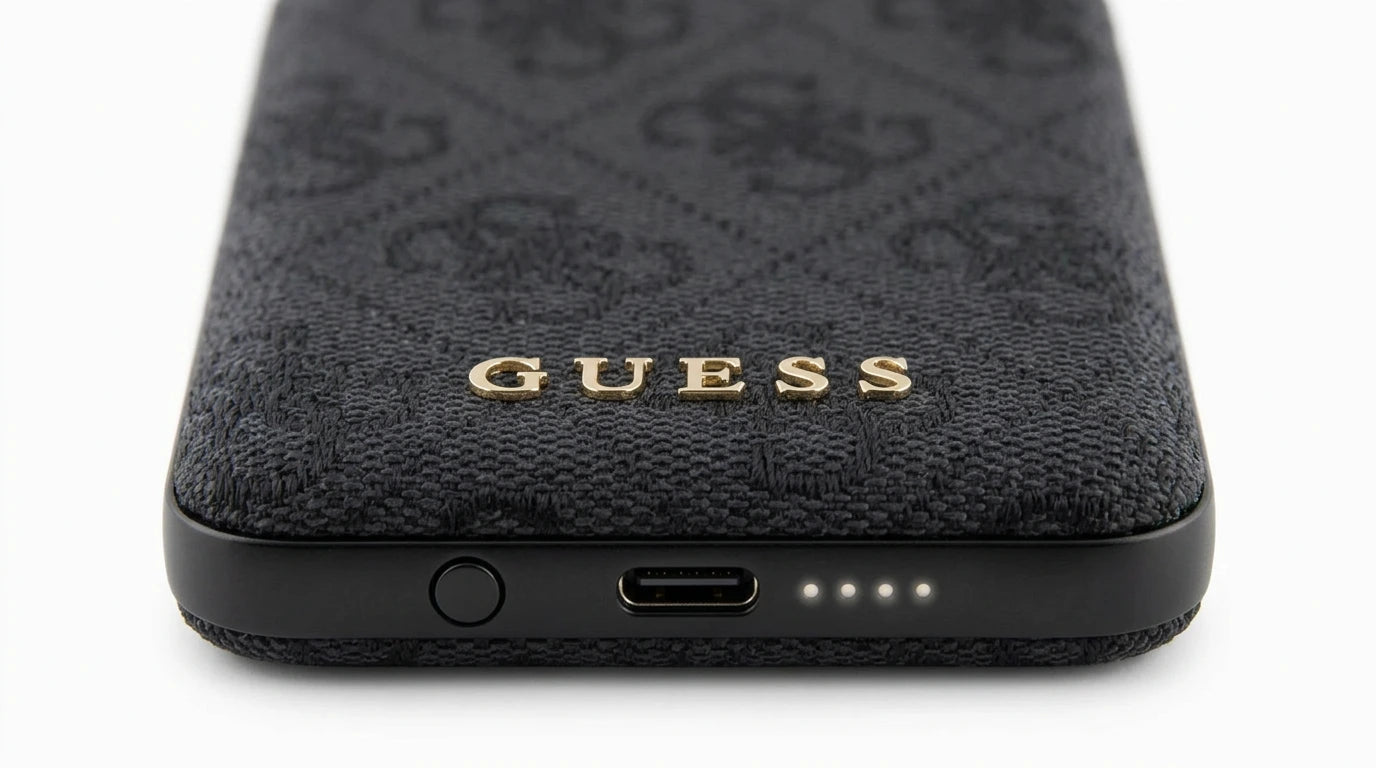 future tech gadgets Canada. premium tech accessories Canada. Guess BP MagSafe Case + PWB 5000mAh 4G. Gallery image 9. The image shows a close-up view of a dark, textured phone case, prominently featuring a gold "GUESS" logo at the center. The case has a woven fabric appearance with a subtle pattern, and it is positioned horizontally against a seamless white background. At the bottom edge, a USB-C port is visible alongside three small status LED lights indicating battery level.