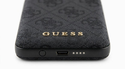 future tech gadgets Canada. premium tech accessories Canada. Guess BP MagSafe Case + PWB 5000mAh 4G. Gallery image 9. The image shows a close-up view of a dark, textured phone case, prominently featuring a gold "GUESS" logo at the center. The case has a woven fabric appearance with a subtle pattern, and it is positioned horizontally against a seamless white background. At the bottom edge, a USB-C port is visible alongside three small status LED lights indicating battery level.