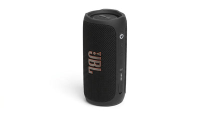 future tech gadgets Canada. smart tech store Canada. JBL Flip 7 Portable waterproof and drop-proof speaker. Gallery image 8. The portable speaker is positioned upright in the center of the frame against a seamless white background. Its body is predominantly black with a textured fabric covering, and it features a prominent JBL logo in copper on the front.