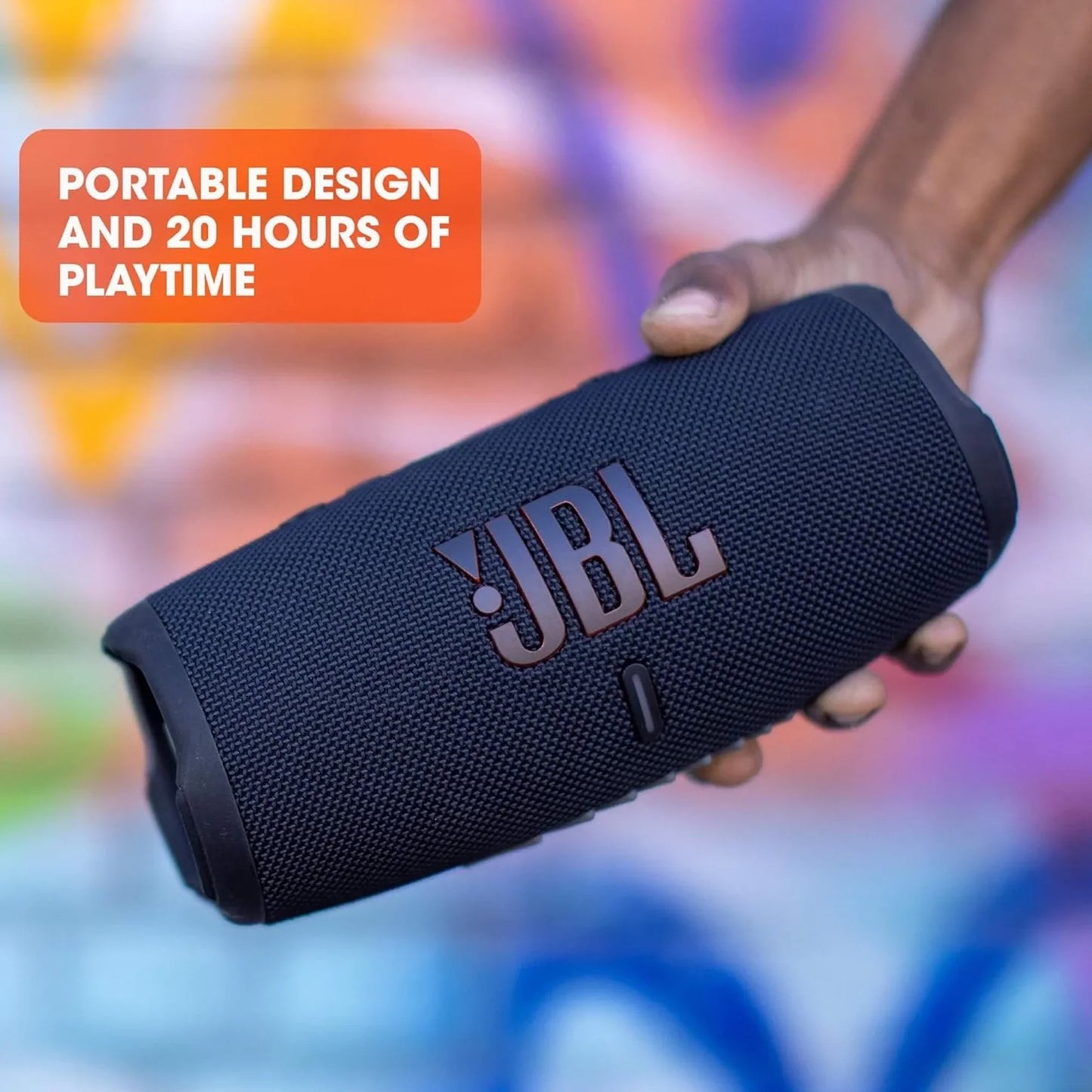 future tech gadgets Canada. premium tech accessories Canada. JBL Charge 5 Portable Waterproof Speaker with Powerbank. Gallery image 5. A black portable speaker is held in a hand, angled slightly to showcase its textured surface and prominent JBL logo. The speaker features a cylindrical shape with a rubberized end and a small button visible on the front. The background is a vibrant, graffiti-style mural with splashes of color, creating a lively atmosphere.
