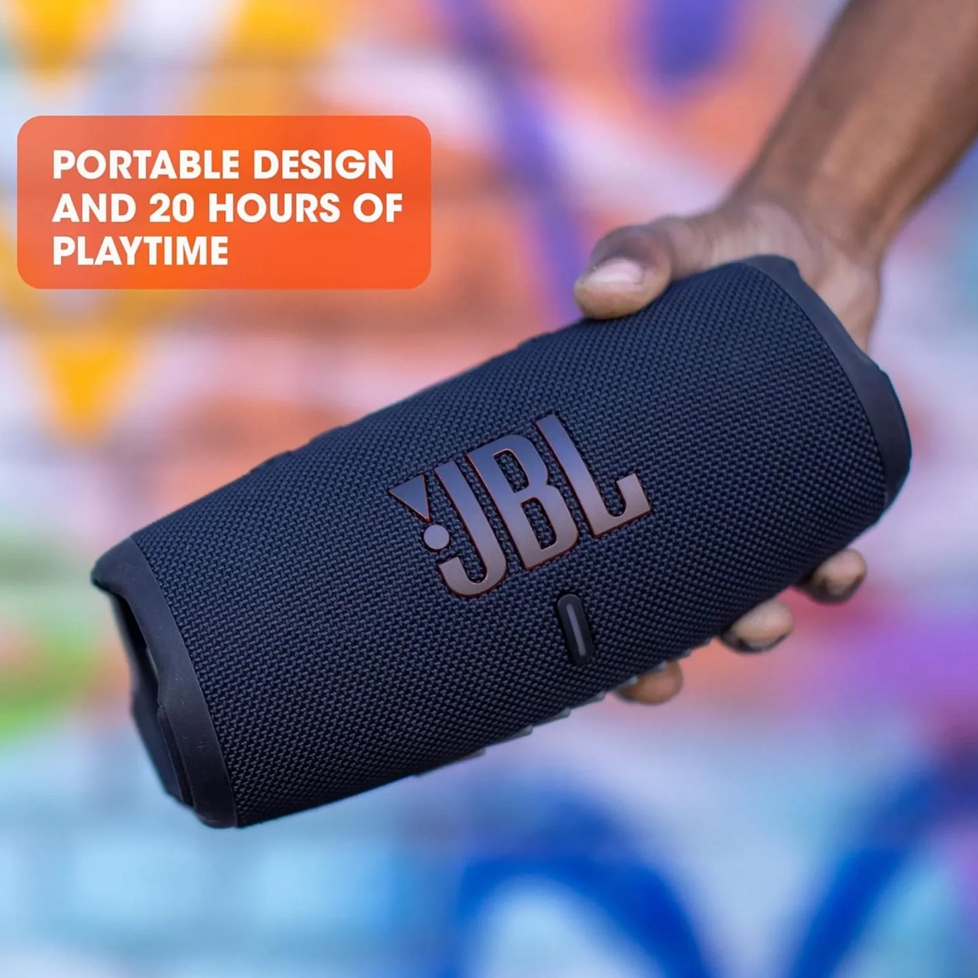 future tech gadgets Canada. premium tech accessories Canada. JBL Charge 5 Portable Waterproof Speaker with Powerbank. Gallery image 5. A black portable speaker is held in a hand, angled slightly to showcase its textured surface and prominent JBL logo. The speaker features a cylindrical shape with a rubberized end and a small button visible on the front. The background is a vibrant, graffiti-style mural with splashes of color, creating a lively atmosphere.