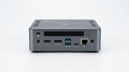 future tech gadgets Canada. gaming handheld PC Canada. Machenike GTX PH94H28 Mini PC. Gallery image 5. The product is a compact gray computer unit, positioned centrally against a seamless white background. The camera captures the rear view, showcasing various ports and connectors, including HDMI, DisplayPort, USB 3.0/3.1, and USB Type-C. The surface has a matte finish, with subtle highlights reflecting the soft studio lighting.