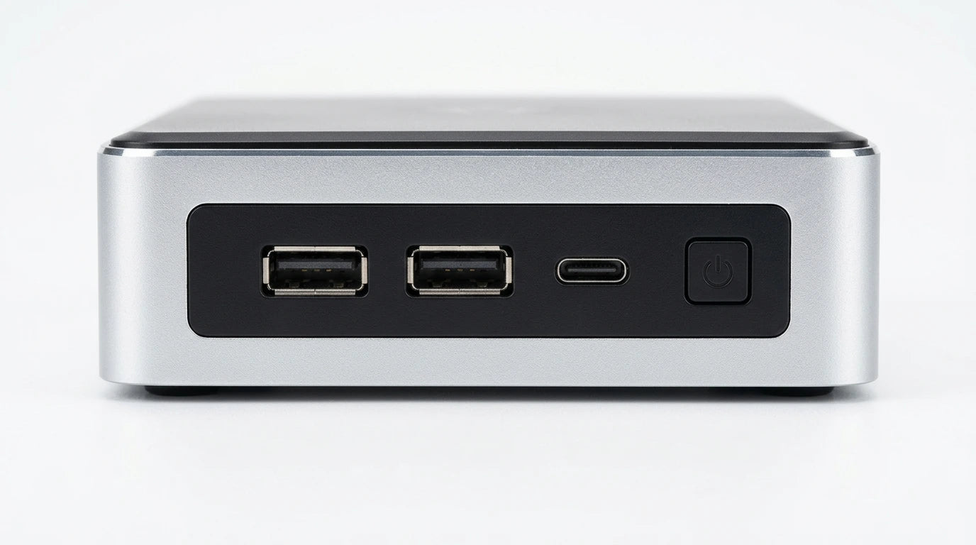 future tech gadgets Canada. gaming handheld PC Canada. Machenike GTX PH94H28 Mini PC. Gallery image 8. The product is positioned centrally in the frame, showcasing its front view against a seamless white background. The unit features a sleek, brushed silver finish with a matte black panel that houses two standard USB ports and a USB-C port. To the right, there is a prominent power button. The lighting is bright and even, highlighting the clean lines and modern design of the device.