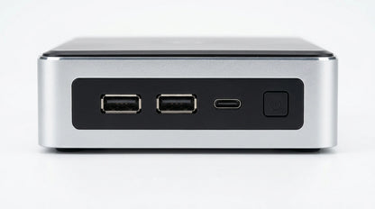 future tech gadgets Canada. gaming handheld PC Canada. Machenike GTX PH94H28 Mini PC. Gallery image 8. The product is positioned centrally in the frame, showcasing its front view against a seamless white background. The unit features a sleek, brushed silver finish with a matte black panel that houses two standard USB ports and a USB-C port. To the right, there is a prominent power button. The lighting is bright and even, highlighting the clean lines and modern design of the device.