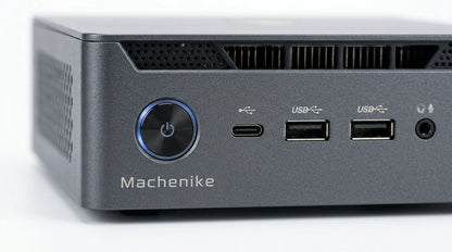 future tech gadgets Canada. smart tech store Canada. Machenike GTX PH94H48 Mini PC. Gallery image 9. The product is a compact gray desktop computer, positioned at an angle in the frame, showcasing its front panel. The surface is a smooth white backdrop, enhancing the product's sleek design. The lighting is bright and even, highlighting the matte finish of the body.