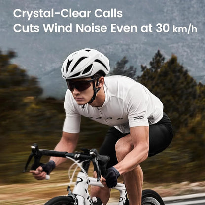 future tech gadgets Canada. smart tech store Canada. Mojawa Purra Run Bone Conduction Running Headphones. Gallery image 7. A cyclist is captured in motion, leaning forward on a sleek white bicycle with black accents. He wears a fitted white short-sleeve jersey and black shorts, complemented by a white helmet and dark sunglasses. The background features blurred greenery and mountains, suggesting a dynamic outdoor setting.
