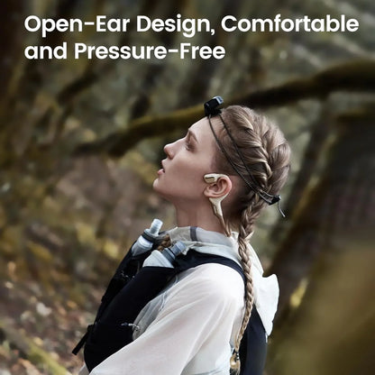 future tech gadgets Canada. smart tech store Canada. Mojawa Purra Run Bone Conduction Running Headphones. Gallery image 8. A woman with a braided hairstyle is shown in profile, wearing open-ear headphones that have a sleek, gold and white design. She is dressed in a light, breathable top and a black vest with pockets, suggesting an outdoor or athletic setting. The background features blurred greenery, indicating a natural environment.