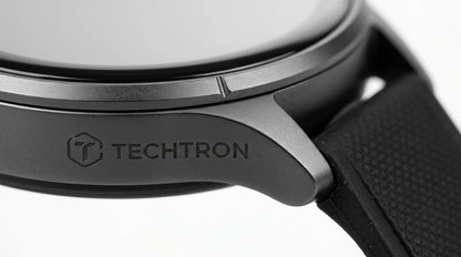 smart tech store Canada. premium tech accessories Canada. Techtron Aurafit AM23 Smart Watch. Gallery image 5. The image features a close-up view of a smartwatch, angled slightly to showcase its design. The watch has a sleek, matte black body with a smooth, circular glass face. Prominently displayed on the side is the engraved logo "TECHTRON," which is set against a textured surface. The background is a seamless white, enhancing the watch's modern aesthetic.