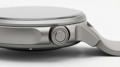 smart tech store Canada. premium tech accessories Canada. Techtron Aurafit AM23 Smart Watch. Gallery image 9. The image shows a close-up view of a sleek, silver watch positioned at an angle against a seamless white background. The watch features a smooth, glossy glass face and a brushed metal body, highlighting its modern design. Prominently displayed on the right side is a textured crown for adjusting settings, accompanied by a smaller, circular button beneath it.