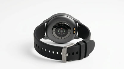 smart tech store Canada. premium tech accessories Canada. Techtron Aurafit AM28 Smart Watch. Gallery image 6. The image shows the back of a smartwatch positioned centrally against a seamless white background. The watch features a round, glossy black case with a circular sensor area in the middle, surrounded by small colored lights. The strap is made of matte black rubber, with a metal buckle on the right side. The overall lighting is soft, highlighting the watch's details without harsh shadows.